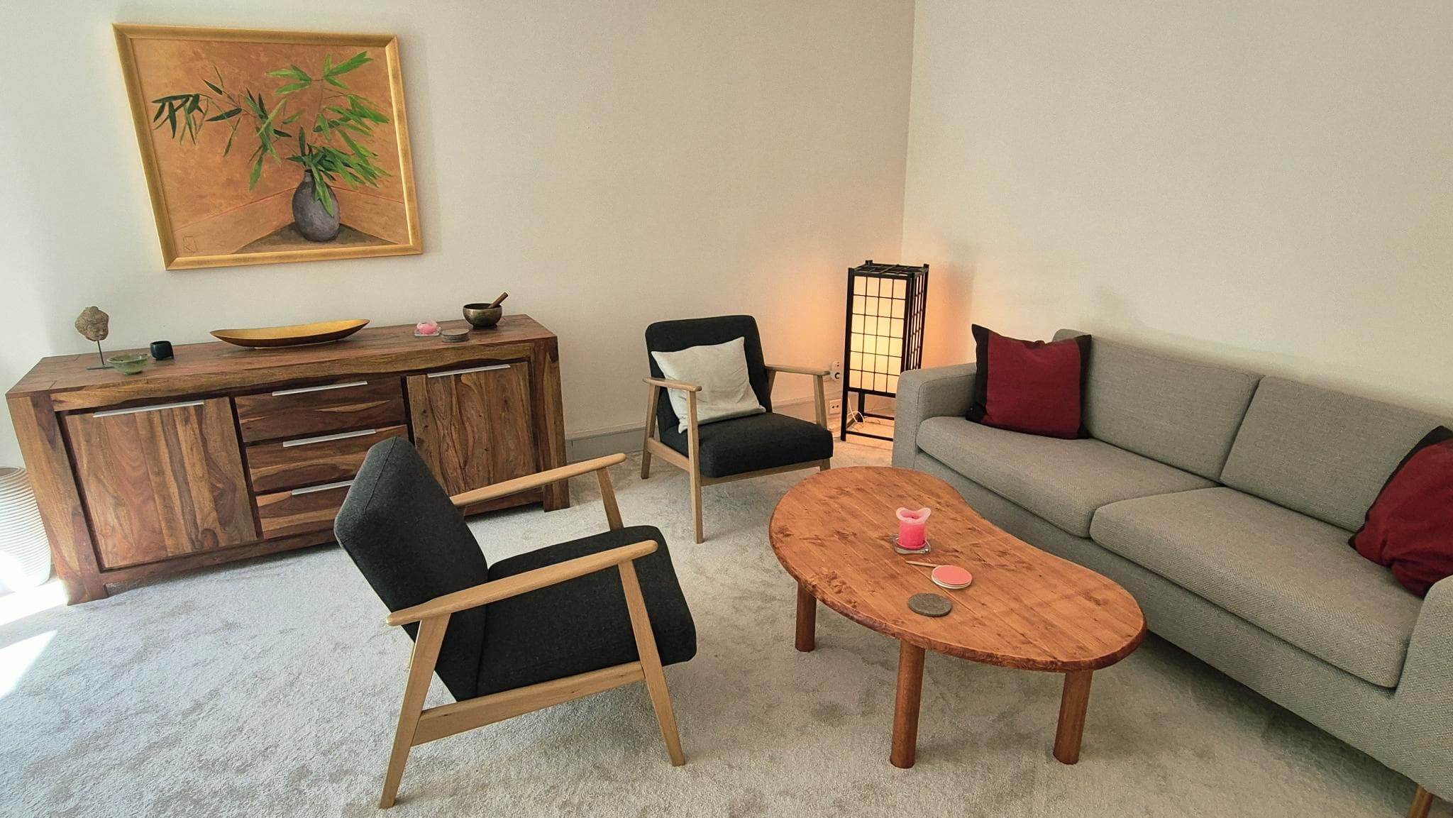 Heller Beratungsraum in Hamburg-Harvestehude mit grauem Sofa, zwei Sesseln, einem nierenförmigen Holztisch und einer Holzkommode